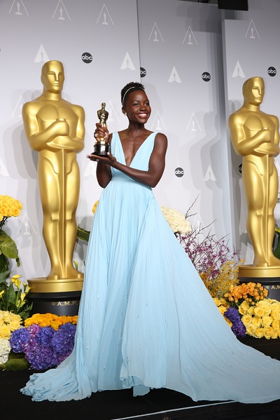 Lupita Nyong'o wearing a beautiful light blue evening gown, holding her Oscar Award.