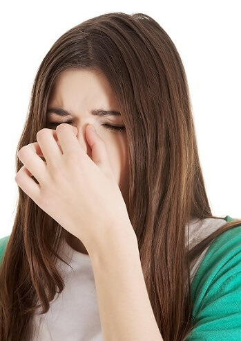 A woman pinching the bridge of her nose, indicating sinus discomfort or headache.